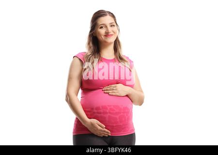 Schwangere Frau in rosa Oberteil und Leggings lächelt und hält ihren Bauch isoliert auf weißem Hintergrund Stockfoto