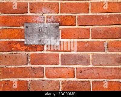 Frontale und formatfüllende Sicht auf eine Ziegelwand mit verwittertem Metallschild. Stockfoto