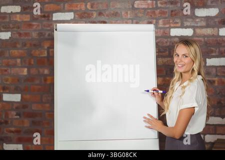 Frau in Geschäftskleidung präsentiert leere Flipchart im Büro mit violettem Marker, Kopierraum Stockfoto