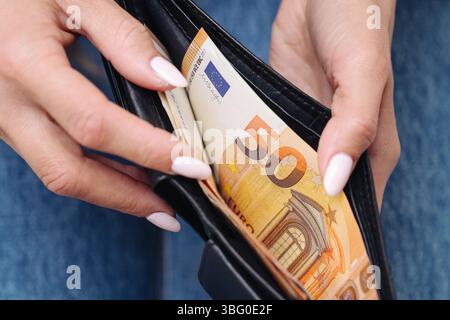 Brieftasche mit Euro halten. Frau mit Maniküre zeigt 50 Euro. Persönliches Finanzierungskonzept. Nahaufnahme der schwarzen Ledertasche. Weibliche Hände und Geld. Stockfoto