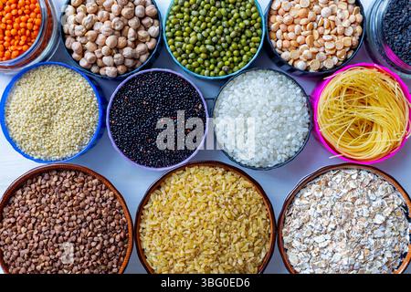Verschiedene Trockenkörner, Hülsenfrüchte und Nudeln in farbenfrohen Schüsseln. Ein Blick von oben auf verschiedene Trockenkörner, Hülsenfrüchte und Pastagerichte, die in bunten Schüsseln auf einem angeordnet sind Stockfoto
