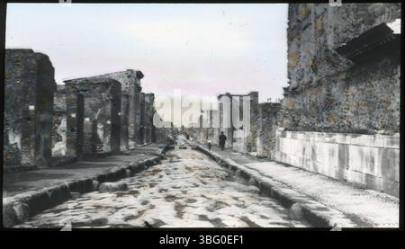 Ein Mann und ein Kind spazieren entlang der Via della Fortuna in Pompeji, Italien, die während der Europatour der Arrases 1913 festgehalten wurde. Die Straße führt durch die antike Stadt und ist eine von vielen Straßen, die an historischen Stätten wie dem Tempel des Glücks vorbeiführen. Stockfoto