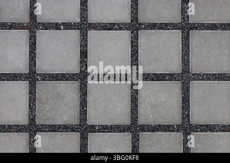 Quadratische, graue Fliesen auf einem Substrat aus kleinen, schwarzen Steinen Hintergrund Stockfoto