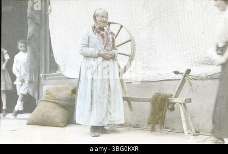 Eine Frau, die an ihrem drehenden Rad auf der High Street in Kenmare, Irland, stand und 1913 während der Europatour der Arrases gefangen genommen wurde. Das Foto bietet einen Einblick in das ländliche Leben und die traditionelle Handwerkskunst in Irland während dieser Zeit. Stockfoto