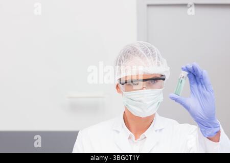 Wissenschaftler, der kleine transparente Fläschchen mit blassgrüner Flüssigkeit im Labor am grauen Schrank hält Stockfoto