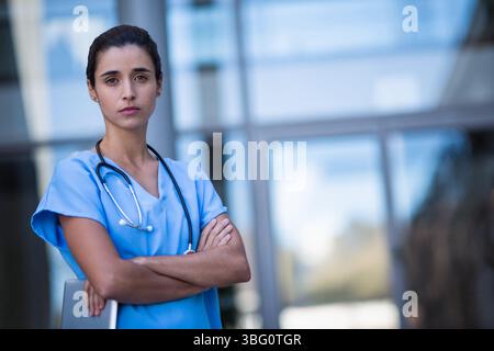 Weibliche Krankenschwester, die außerhalb des Krankenhauses steht, trägt Peelings mit Tablette und Stethoskop, Kopierraum Stockfoto