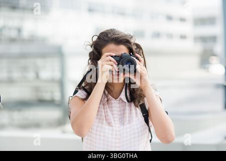 Fotografin, die DSLR-Kamera auf der Dachterrasse mit Metallgeländern und verschwommenen Fassaden hochhebt Stockfoto
