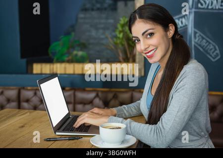 Frau tippt auf Laptop am Coffee-Shop-Tisch mit Kaffeetasse und Bambuspflanzen, Kopierraum Stockfoto