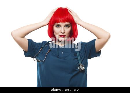 Schöne glückliche, fröhliche Frau Doktor, die in die Kamera schaut lustiges Zeichen mit roter Perücke, die Haare mit ihren Händen hält Stockfoto