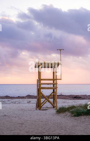 Leerer hölzerner Rettungsschwimmerturm an einem Sandstrand bei Sonnenuntergang. Ruhige Küstenszene, Soft Sky, Horizont Meereslandschaft, friedliche Abendatmosphäre in Punta Prim Stockfoto