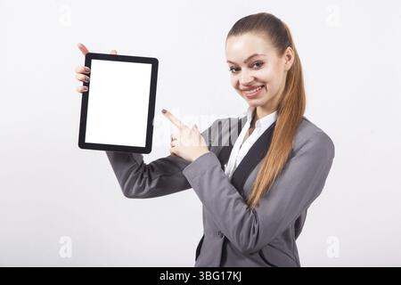 Moderne junge Geschäftsfrau in einem Business-Anzug auf weißem Hintergrund zeigt in den Händen des Tablets vertikal den Bildschirm nach vorne und zeigt mit dem Finger auf den Bildschirm Stockfoto