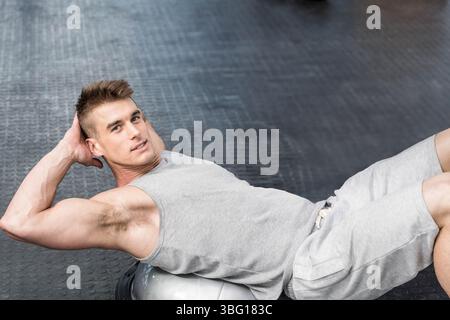 Der Mann macht Bauchknirschen am BOSU-Trainer auf dunklem Gummi-Fitnessboden, fokussiert auf den Kern Stockfoto