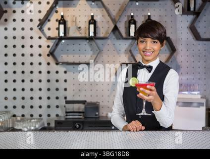 Asiatische Barkeperin hält roten Limettencocktail hinter der Lounge-Theke mit Weinregalen, Kopierraum Stockfoto