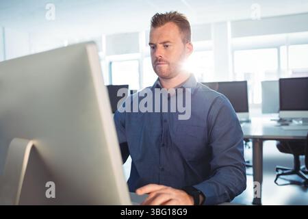 Der Desktop-Monitor leuchtet auf dem Schreibtisch in einem hellen Büro mit leeren Arbeitsplätzen und großen Fenstern Stockfoto
