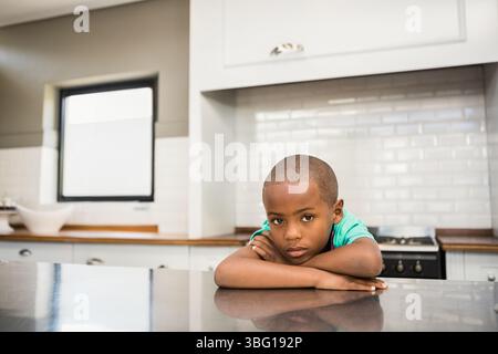 Afroamerikanischer Junge, der sich auf der Kücheninsel mit glänzender Arbeitsplatte nach vorne lehnt und das Kinn auf den Armen auflegt Stockfoto