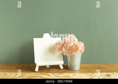 Staffelei und leere Leinwand mit Nelkenblumen auf Holztisch. Grüner Hintergrund Stockfoto