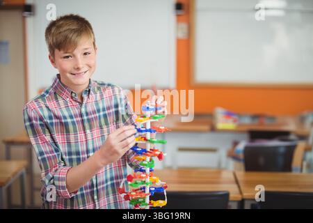 Schuljunge lächelt und baut buntes DNA-Modell aus Plastik auf dem Schreibtisch im Klassenzimmer, Kopierraum Stockfoto