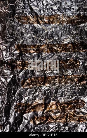 Reflektierender silberner Hintergrund mit zerknittertem Alufolie-Muster und horizontalen braunen Mustern Stockfoto