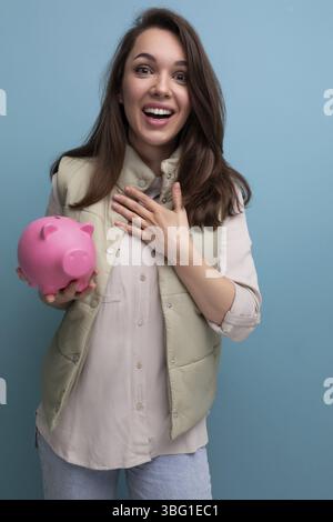 Glückliche junge brünette Frau, die rosa Spargeld hält Stockfoto