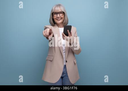 Reife Frau in einem stilvollen Bild mit einem Smartphone in der Hand auf einem Studiohintergrund mit Kopierraum Stockfoto