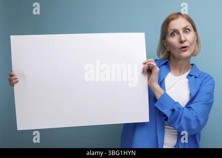 Geschäftskonzept mittleren Alters. Frau mittleren Alters, die ein Poster für Notizen mit einem Mocap auf einem blauen Hintergrund hält Stockfoto