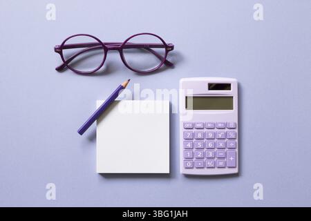 Notizblock, Buntstift, Taschenrechner, Brille auf violettem Hintergrund. Arbeitsbereich. Flach liegend, Draufsicht Stockfoto