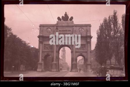 Das Siegestor in München, erbaut 1852, steht als Triumphbogen. Dieses Foto, das während der Europatour der Arrases 1913 aufgenommen wurde, zeigt Fußgänger, Automobile und Trolley-Autos, die unter dem historischen Gebäude vorbeifahren, was seine Rolle als Verkehrsknotenpunkt in München unterstreicht. Stockfoto