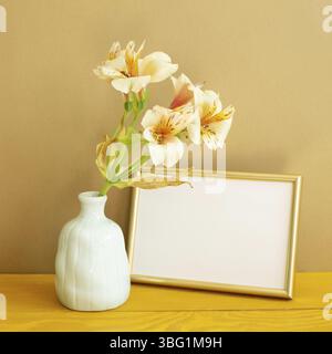 Leerer Bilderrahmen mit Blumen auf Holztisch. Brauner Hintergrund Stockfoto