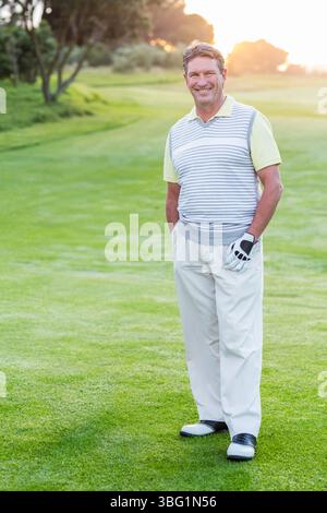 Ranghoher Afroamerikaner, der bei Sonnenuntergang auf dem Golf Fairway steht und Golfhandschuh trägt, Pullover Weste Stockfoto