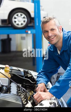 Mittelgroßer Mann in Overalls, der sich über die geöffnete Haube beugt und den Motor in der Werkstatt überprüft, im Kopierraum Stockfoto