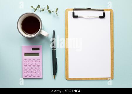 Arbeitsbereich. Zwischenablage und leeres Blatt Papier und Rechner mit Tasse Kaffee auf blauem Hintergrund. Draufsicht Stockfoto