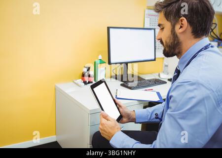 Männlicher Arzt, der am Schreibtisch in der Nähe der gelben Wand sitzt und ein Stethoskop in der Nähe des Monitors trägt Stockfoto
