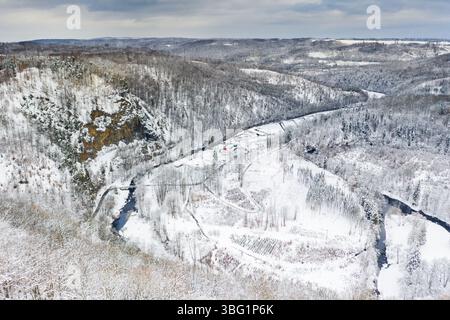 Aus der Vogelperspektive auf ein schneebedecktes Dorf und die umliegende Winterlandschaft in der Landschaft mit gewundenen Fluss und Hügeln mit Bäumen Stockfoto