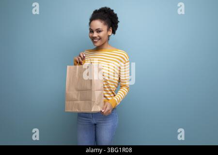 Afro Brünette latein, junge Frau, die eine handwerkliche Geschenktüte hält Stockfoto