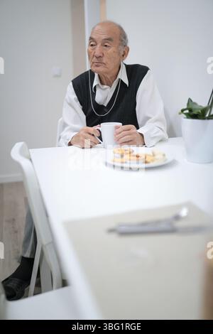Seniorin genießt Frühstück mit kabellosen Kopfhörern zu Hause Stockfoto