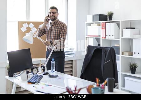 Ein bärtiger Mann in kariertem Hemd, Brille und dunkler Hose arbeitet in einem hellen Büro. Foto mit Schärfentiefe Stockfoto