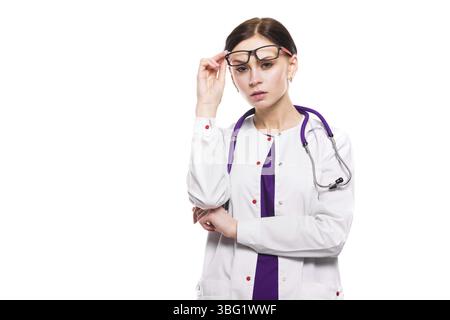 Porträt einer jungen attraktiven ernsthaften Ärztin, die im Büro steht und auf einen in der Kamera schaut, in weißer Uniform kaukasische Brünette wartet Stockfoto
