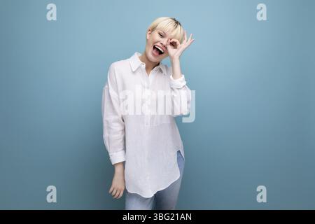 Junge schöne blonde Büroangestellte Frau mit bob-Frisur und gekleidet in weißem Hemd isoliert auf blauem Hintergrund Stockfoto