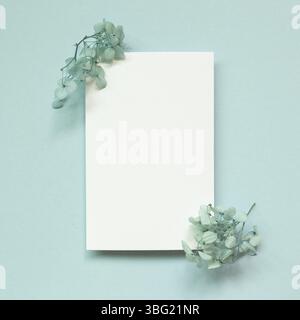 Leeres weißes Notizpapier mit trockenen Blumen auf blauem Hintergrund. Draufsicht, Kopierraum Stockfoto