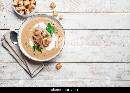 Pilzcremesuppe in der Schüssel garniert mit Croutons und Kräutern auf hölzernem Hintergrund, Draufsicht, Kopierraum. Champignon-Pilzsuppe im Herbst. Stockfoto