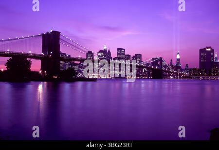 Die Skyline von 2003 in NYC leuchtet in der Abenddämmerung sanft, wenn zwei Lichtstrahlen an der Stelle aufsteigen, an der einst die Towers standen. Der Hudson fließt vorne, was ein düsteres noch widerspiegelt Stockfoto