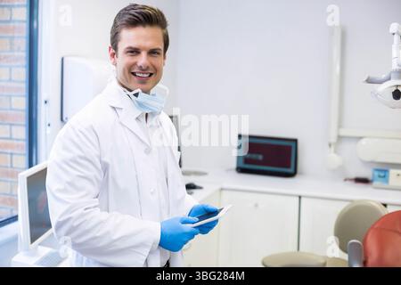 Männlicher Zahnarzt, der Tablette im zahnärztlichen Behandlungsraum mit weißem Mantel und Maske, Kopierraum untersucht Stockfoto