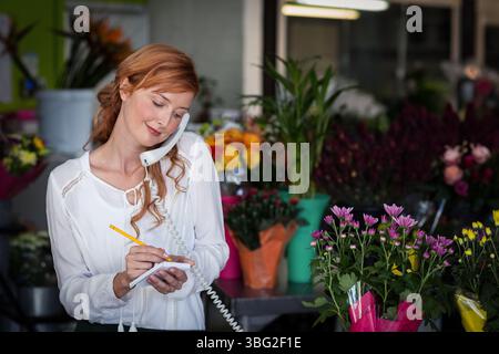 Schnurgebundenes Telefon, das auf dem Ladentisch im Blumenladen liegt, inmitten farbenfroher Topfblumen Stockfoto