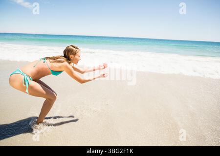 Wellen schlagen auf nassen Sand unter klarem blauen Himmel, Sonnenlicht leuchtet auf türkisfarbenem Wasser Stockfoto