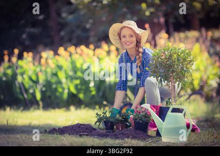 Frau, die auf Gras knien und Blumen mit Gießkanne im sonnendurchfluteten Garten pflanzt, Kopierraum Stockfoto