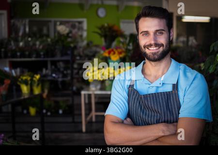 Männlicher Blumenhändler, der im Blumenladen steht, mit gestreifter Schürze, mit Eimern voller Blumen, Kopierraum Stockfoto