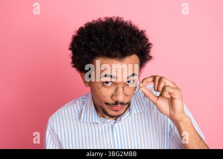 Junger, stilvoller Mann, der die Brille auf rosafarbenem Hintergrund anpasst, der selbstbewussten und trendigen Geschäftsstil mit Eleganz demonstriert Stockfoto