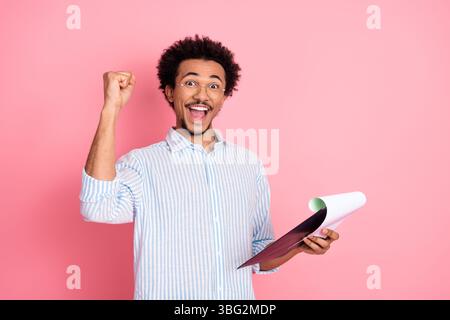 Begeisterte junge Profis, die Dokumente mit fröhlicher Geste vor einem leuchtend rosa Hintergrund halten Stockfoto