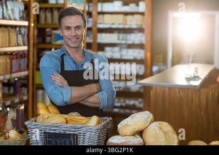 Männlicher Ladenbesitzer mit Schürze, der hinter einem Korb mit Baguettes und Broten auf der Theke in der Bäckerei steht Stockfoto