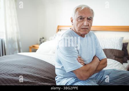 Das Bett ist mit weißen Laken und grauer Steppdecke ausgestattet und verfügt über verschiedene Kissen und eine leuchtende Lampe Stockfoto